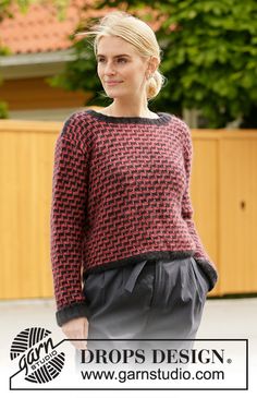 a woman standing in front of a fence wearing a red and black knitted sweater