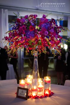 a vase filled with lots of purple and red flowers on top of a white table