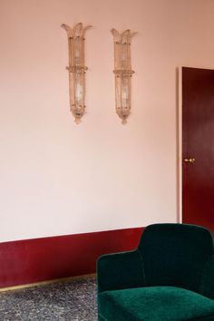 a green chair sitting next to a red door in front of two chandeliers