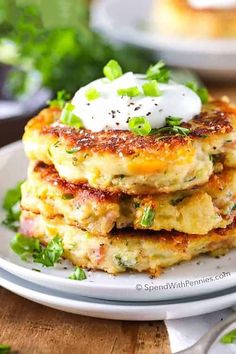 a stack of crab cakes on a plate with sour cream and chives in the background