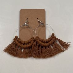 a pair of hoop earrings with tassels on a piece of brown paper next to a clipboard