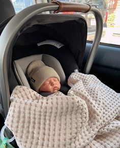 a baby in a car seat with a blanket on it's back and a hat on its head