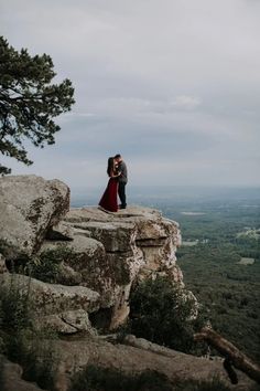 a man and woman standing on top of a rock formation with trees in the background