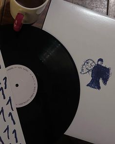 a coffee cup and some vinyl records on a wooden table with an angel sticker