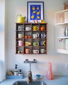 a kitchen sink sitting under a wooden shelf filled with cups