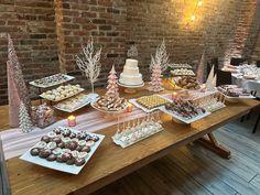 a wooden table topped with lots of desserts and pastries next to a brick wall