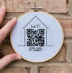 a hand is holding up a cross - stitch project with a house and qr code on it