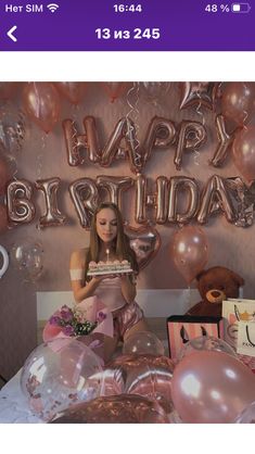 a woman sitting on top of a bed next to balloons and gifts in front of a happy birthday sign