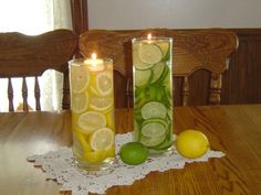 two tall vases filled with lemon and lime slices on top of a wooden table