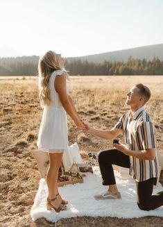 a man kneeling down next to a woman on top of a blanket in the desert