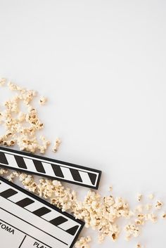 popcorn spilled out of a movie clapper next to a pile of popcorn on a white surface