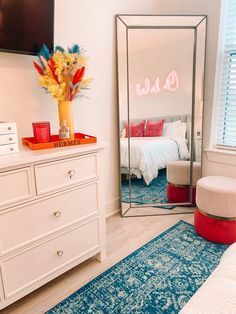 a bedroom scene with focus on the dresser and bed in the background, as well as a large mirror