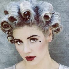 a woman with curly hair and makeup looks at the camera