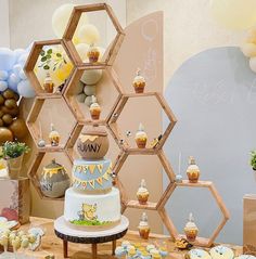 a table topped with cupcakes and cakes next to honeycomb shaped wall decorations