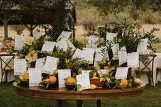 an arrangement of fruit and flowers on a table with seating cards attached to the tables