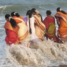 four women in sari are walking into the ocean