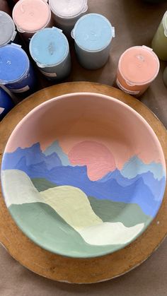 a bowl sitting on top of a wooden table next to paint cans and containers filled with paints