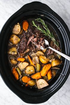 a pot full of stew with carrots, potatoes and meat on the side next to a spoon