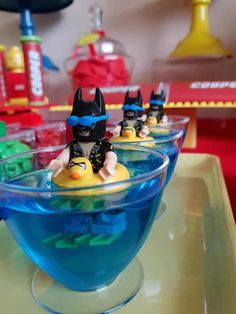 three lego batman toy figures sitting in a blue bowl filled with water on a table