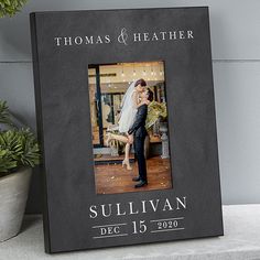 a black frame with a photo of a bride and groom holding each other in front of a potted plant