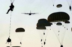 many parachutes are being flown in the sky with an airplane flying overhead behind them