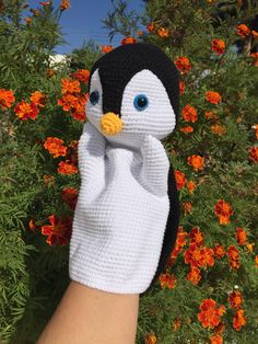 a hand with a knitted penguin on it's palm next to orange flowers