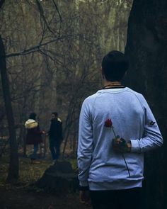 two people standing in the woods with one holding a flower and another looking at something