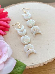 three pairs of earrings sitting on top of a piece of wood next to pink flowers