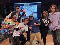 a group of people standing next to each other in front of a tv screen and giving the thumbs up sign