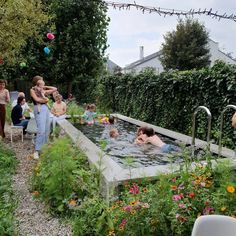 people are gathered around an outdoor hot tub in the garden with flowers and greenery