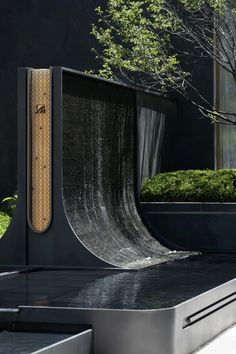 a skateboard ramp in front of a building with a tree and bushes behind it