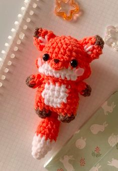 a crocheted red and white stuffed animal laying on top of a notepad