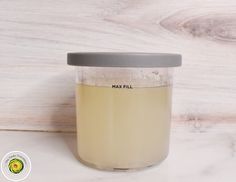 a glass jar filled with liquid sitting on top of a wooden table next to a white wall