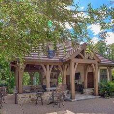 a gazebo with chairs and tables in front of it on a gravel patio surrounded by trees