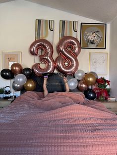 a person laying in bed with balloons and the number twenty eight on top of it