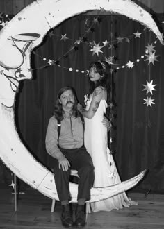 a man and woman pose for a photo in front of a crescent moon with stars