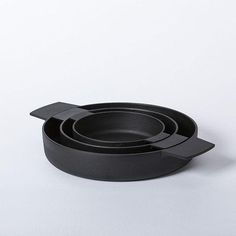 a set of three black bowls on a white surface with one bowl in the middle