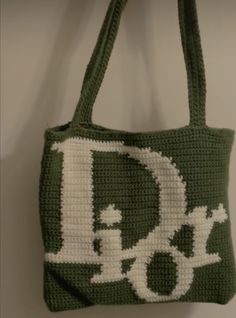 a crocheted bag with the letter d in white and green, hanging on a wall