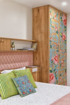 a bed with colorful pillows and wooden headboard next to a closet in a bedroom