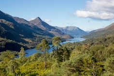 the mountains are covered with trees and water in the distance is a lake surrounded by greenery