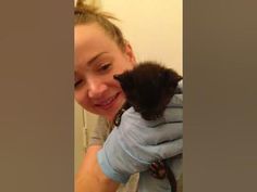 a woman holding a small black animal in her hands and smiling at the camera while wearing blue gloves