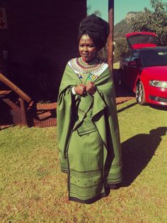 a woman standing in front of a red car wearing a green dress and beaded necklace