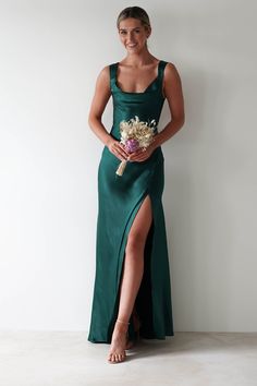 This gown is your perfect choice for debs, prom or any formal event. A look that blends classic glamour with contemporary style. Designed for timeless allure and effortless sophistication. Featuring a graceful cowl neckline and thick shoulder straps, this dress offers a flattering, structured fit. The sultry thigh-high slit adds a bold, modern touch, while the luxurious satin fabric drapes beautifully to enhance your silhouette. Highlights Stunning gown with cowl neckline Soft satin material Ope Satin Emerald Green Bridesmaid Dresses, Green Long Formal Dress, Dark Bridesmaids Dresses, Dark Green Wedding Guest Dress, Wedding Guest Dress 2024, Green Dresses For Wedding, Green Dress Silk, Dark Green Long Dress, Satin Wedding Guest Dress