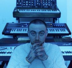 a man is sitting in front of some musical instruments and looking at the camera with his hands on his chin