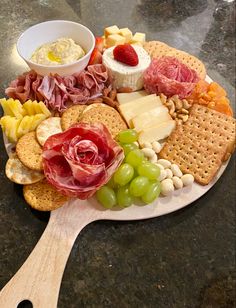 a platter with cheese, crackers, grapes and meats on a wooden spoon