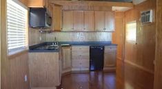 an empty kitchen with wooden cabinets and black counter tops, along with wood flooring