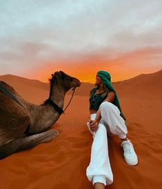 a woman sitting in the desert next to a camel