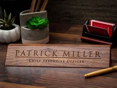 a wooden name plate sitting on top of a table next to a pen and potted plant