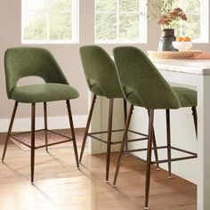 three green chairs sitting on top of a wooden floor next to a white kitchen counter