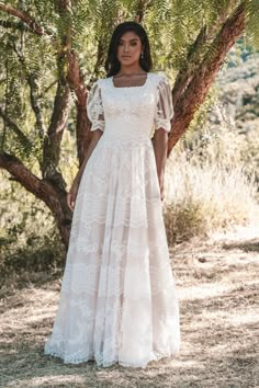 a woman standing in front of a tree wearing a white dress